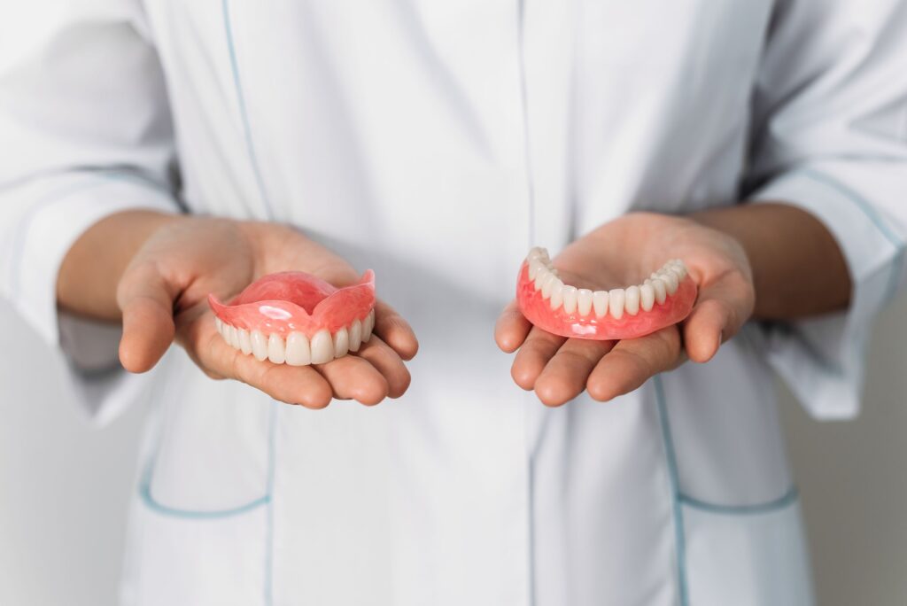 Dentist in white jacket holding a full arch of dentures in each hand