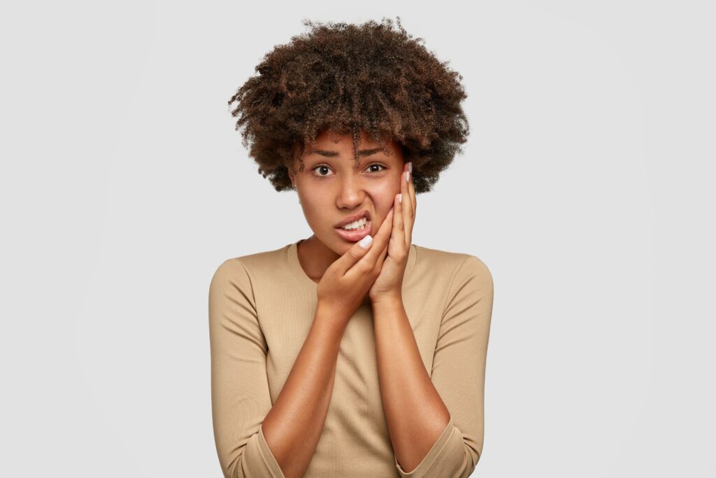 Woman in tan shirt holding both hands to her sore jaw